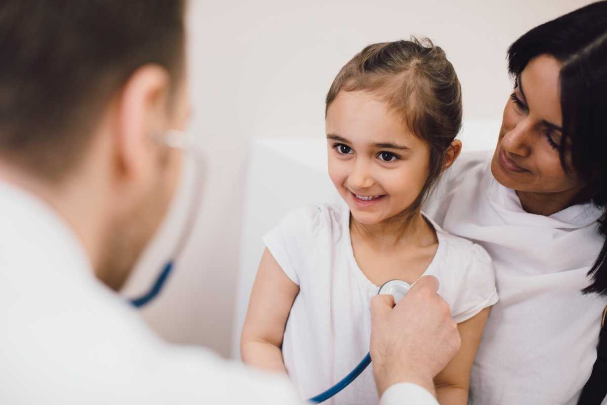 Male pediatrician checking smiling girl in medical clinic