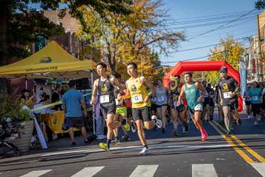 A crowd of runners turning at the first corner of the 2023 QDR Elmhurst Mile in Elmhurst.