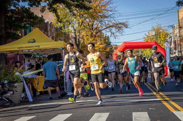 A crowd of runners turning at the first corner of the 2023 QDR Elmhurst Mile in Elmhurst.