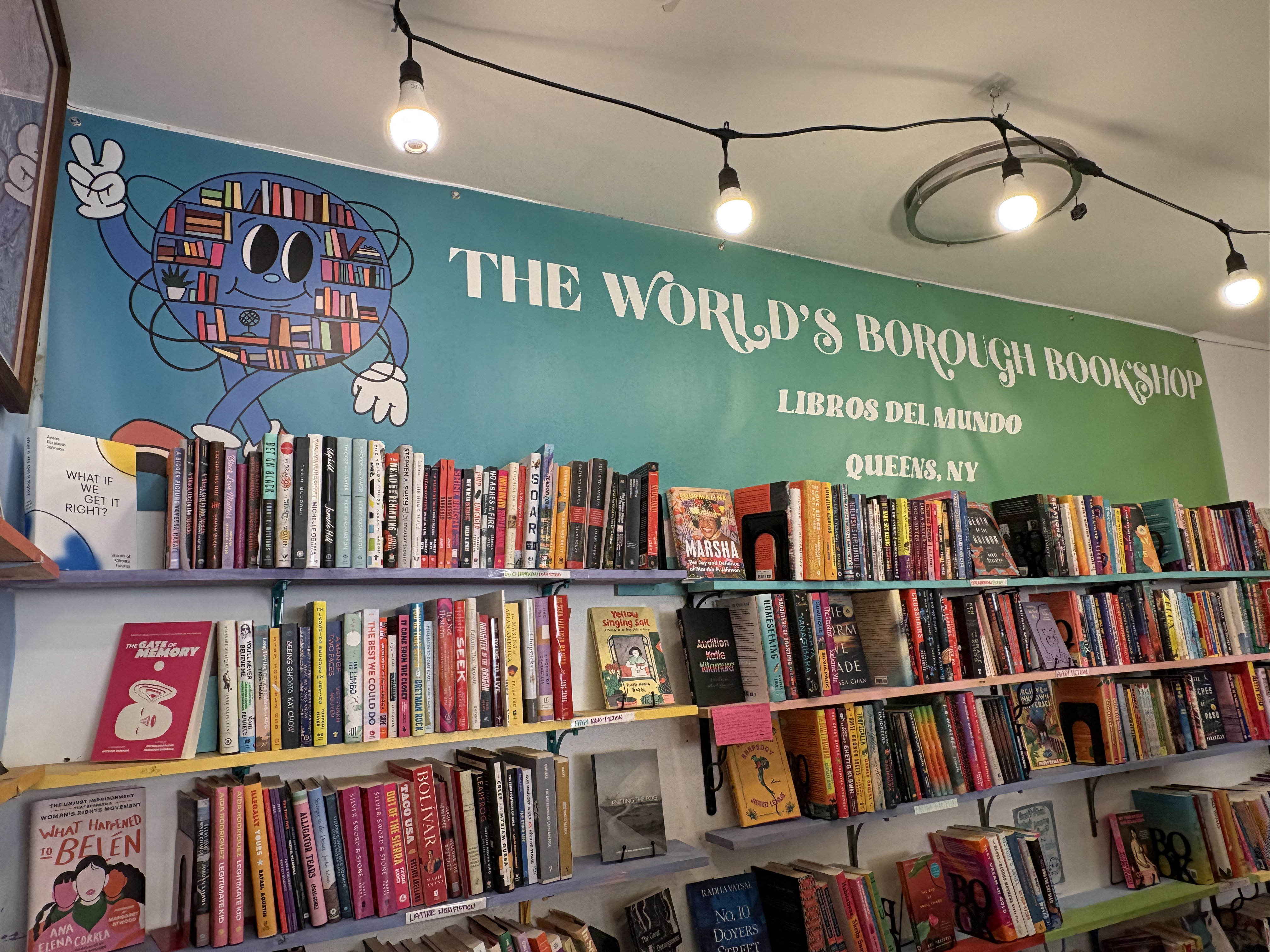 A wall adorned with bookshelves underneath a poster sign at The World's Borough Bookshop in Jackson Heights.