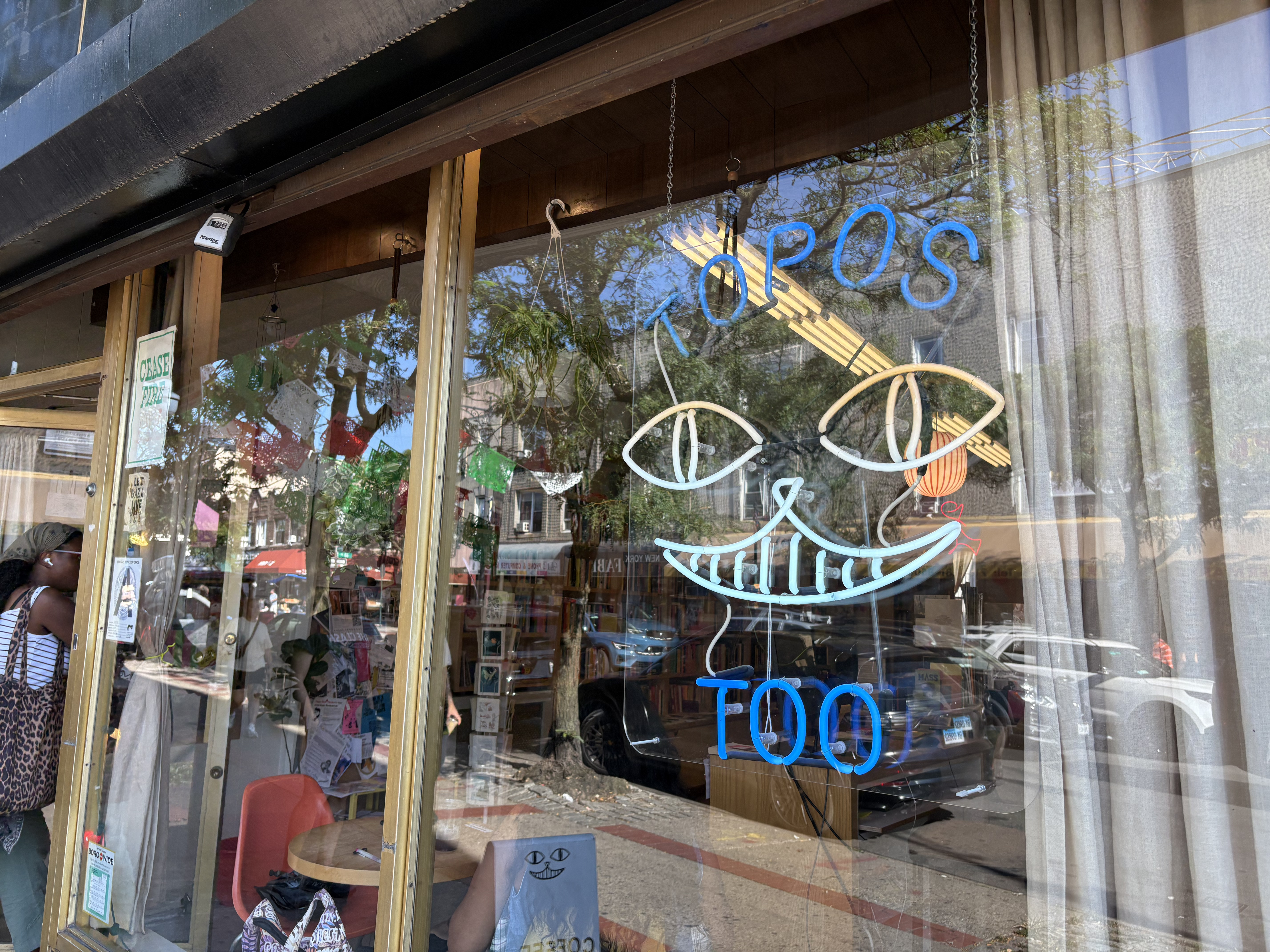 The storefront of Topos Too in Ridgewood, featuring a neon sign on the glass pane.