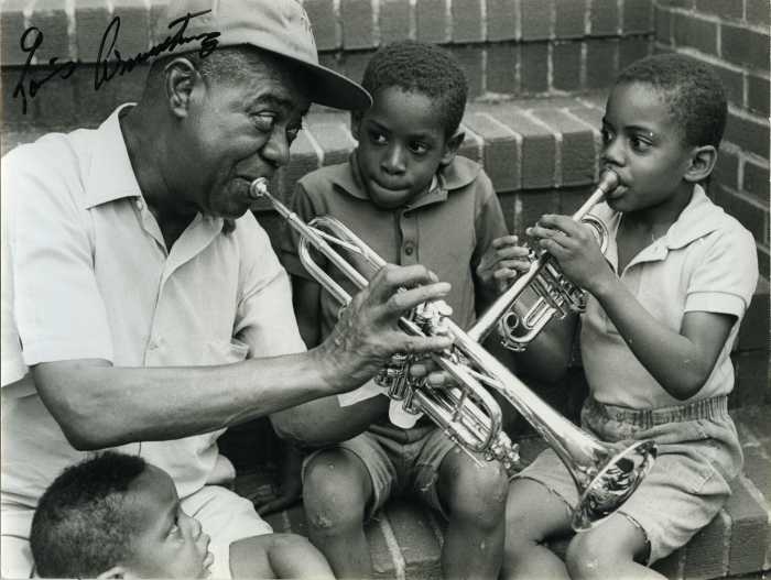 Willie Johnson playing the trumpet with Louis Armstrong, sitting on the Armstrong stoop beside Jonny Johnson and a young child, 1970. Photo Chris Barham / Louis Armstrong House Museum